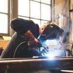 A welder using protective gear in an industrial setting, emitting sparks.